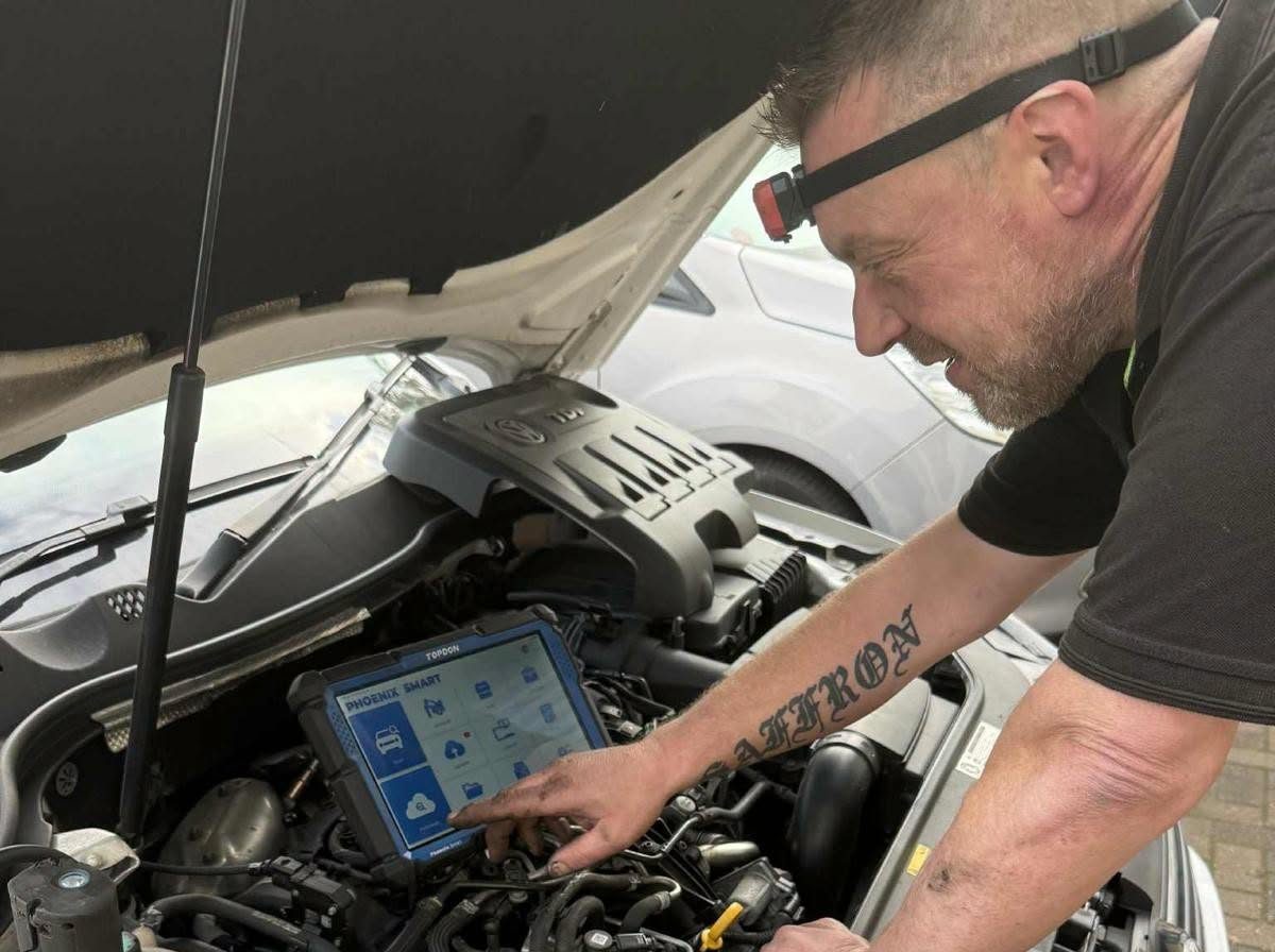 A mechanic plugging a diagnostic tablet in under the bonnet