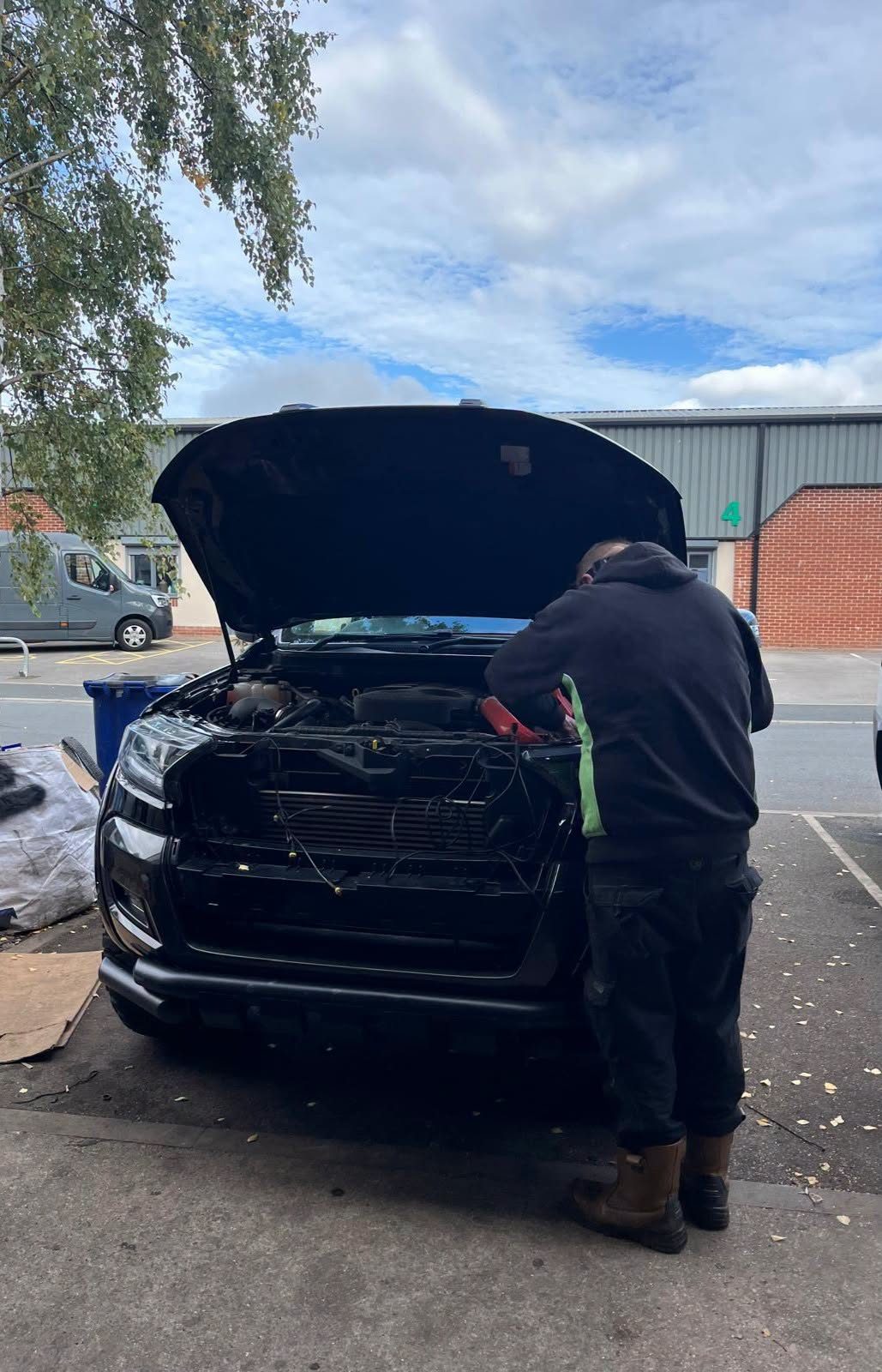 A mechanic working at an open bonnet outside