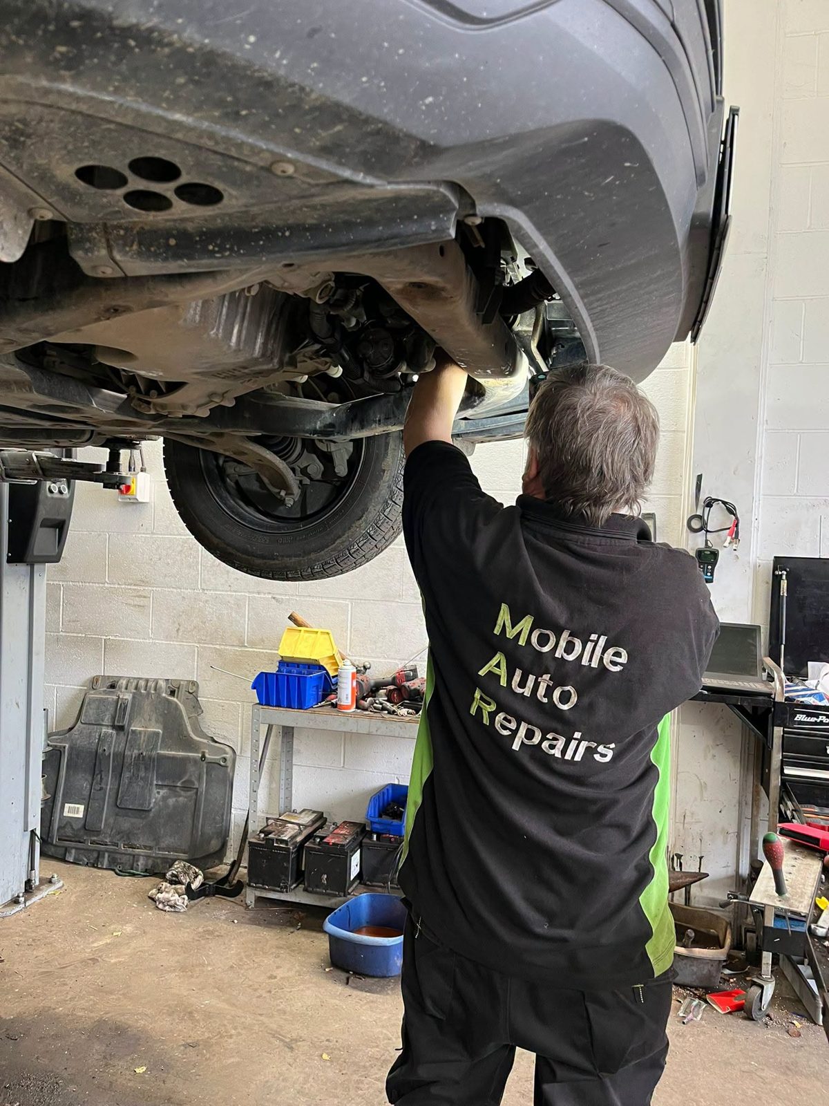 A Mobile Auto Repairs mechanic working underneath a car raised on the lift