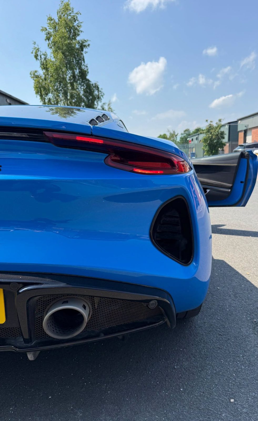 The rear of a blue sports car parked outside the workshop