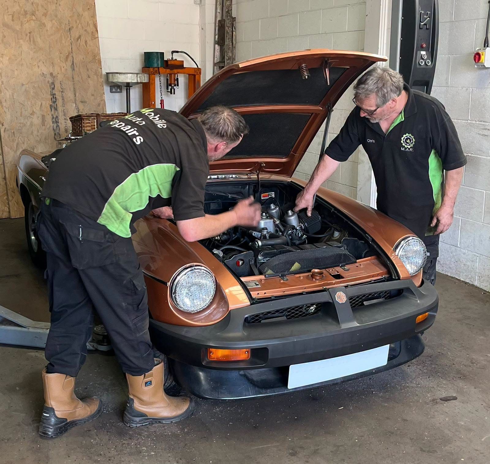 Two of the Mobile Auto Repairs team in their black and green shirts working under the bonnet of a classic MG