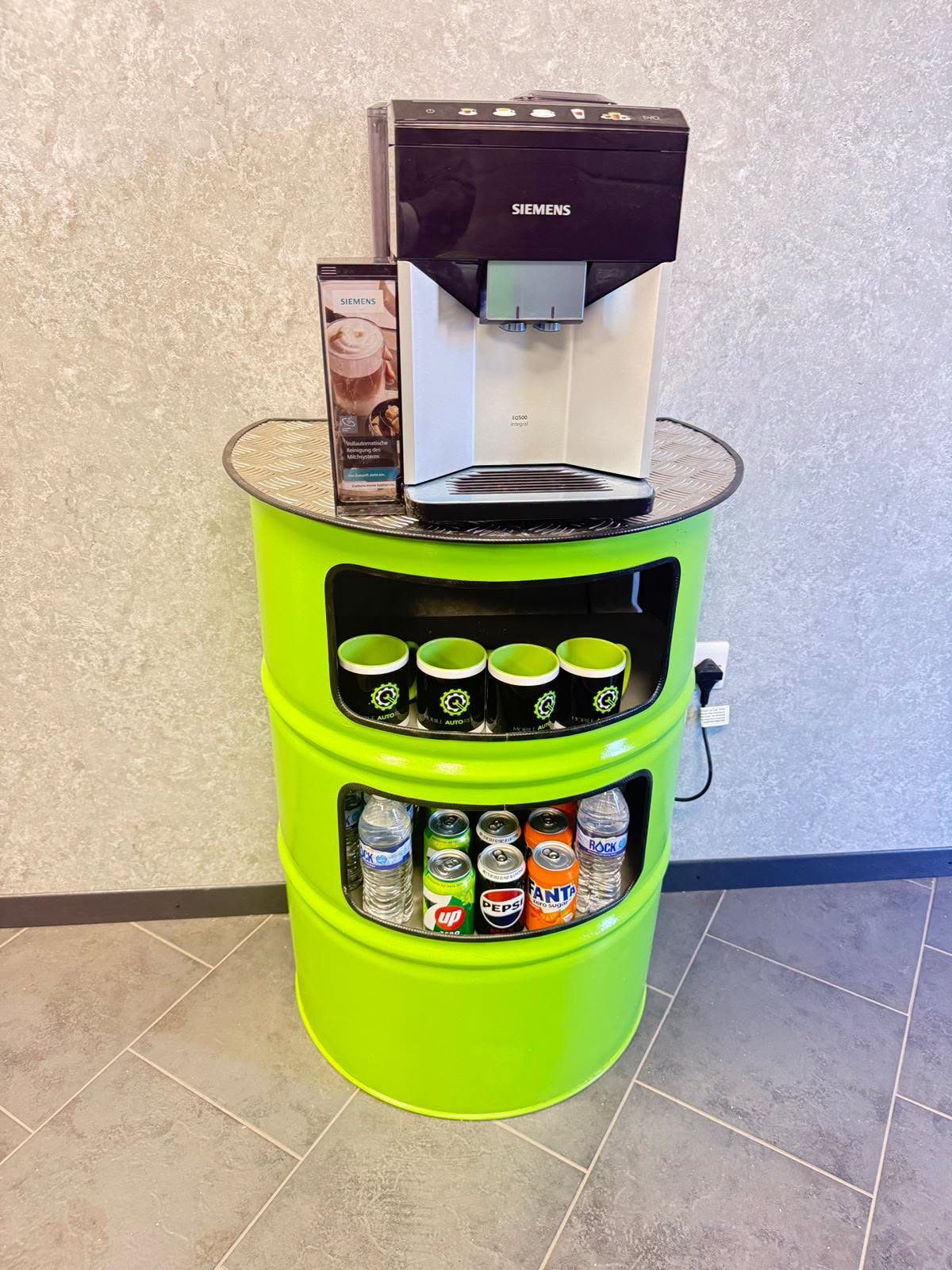 Coffee machine and refreshments on a green barrel stand in the waiting area
