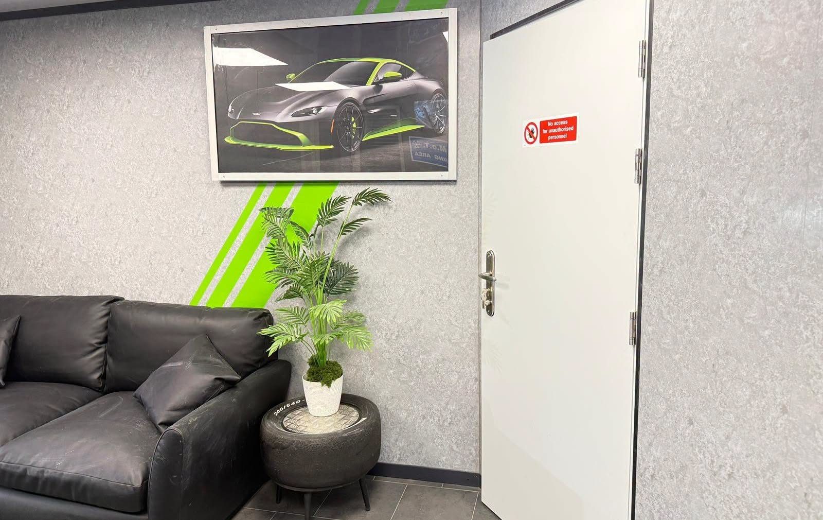 The customer waiting area with a leather sofa, a plant and a green stripe on the wall