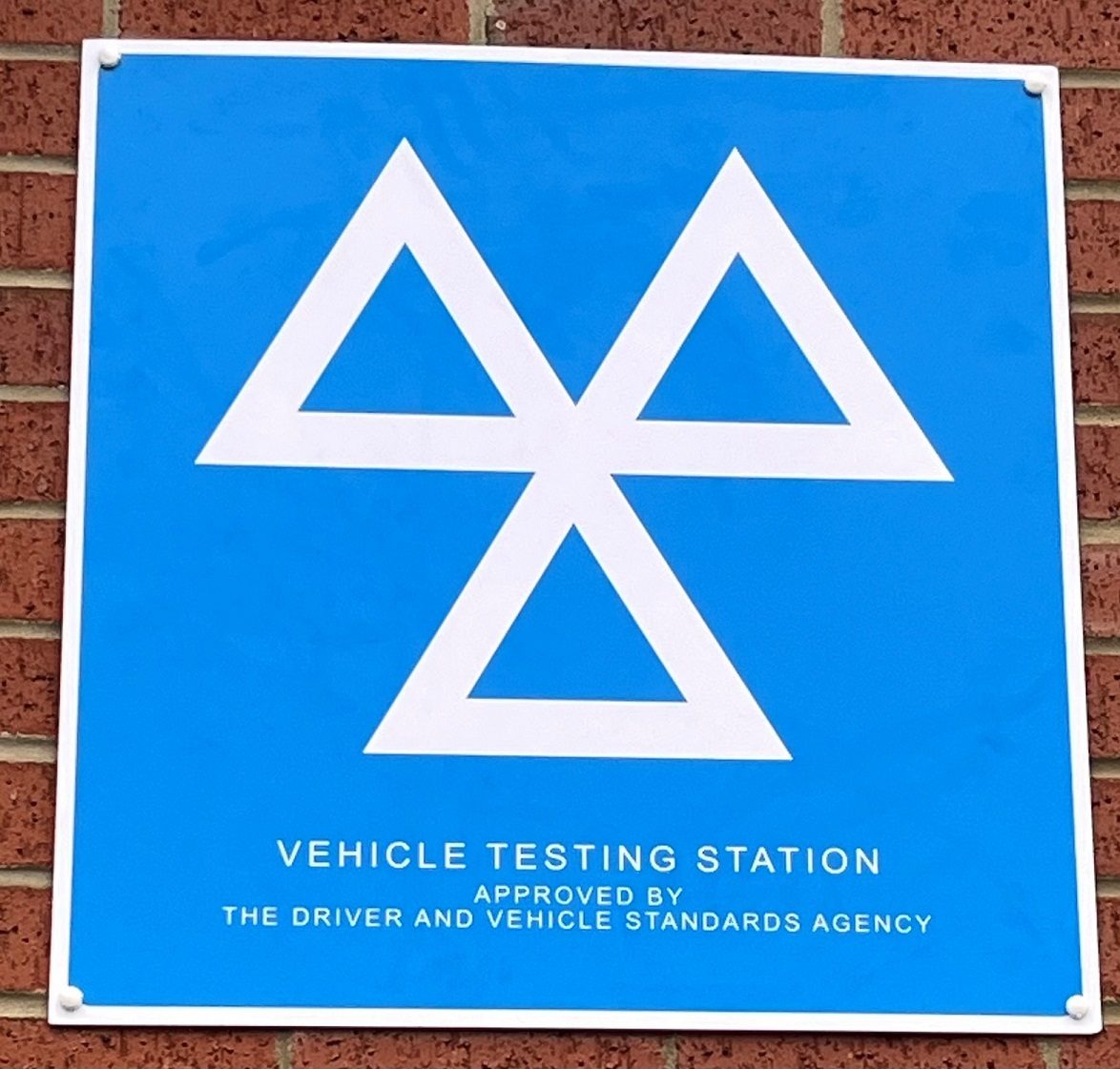 The blue Vehicle Testing Station sign on the wall at Mobile Auto Repairs